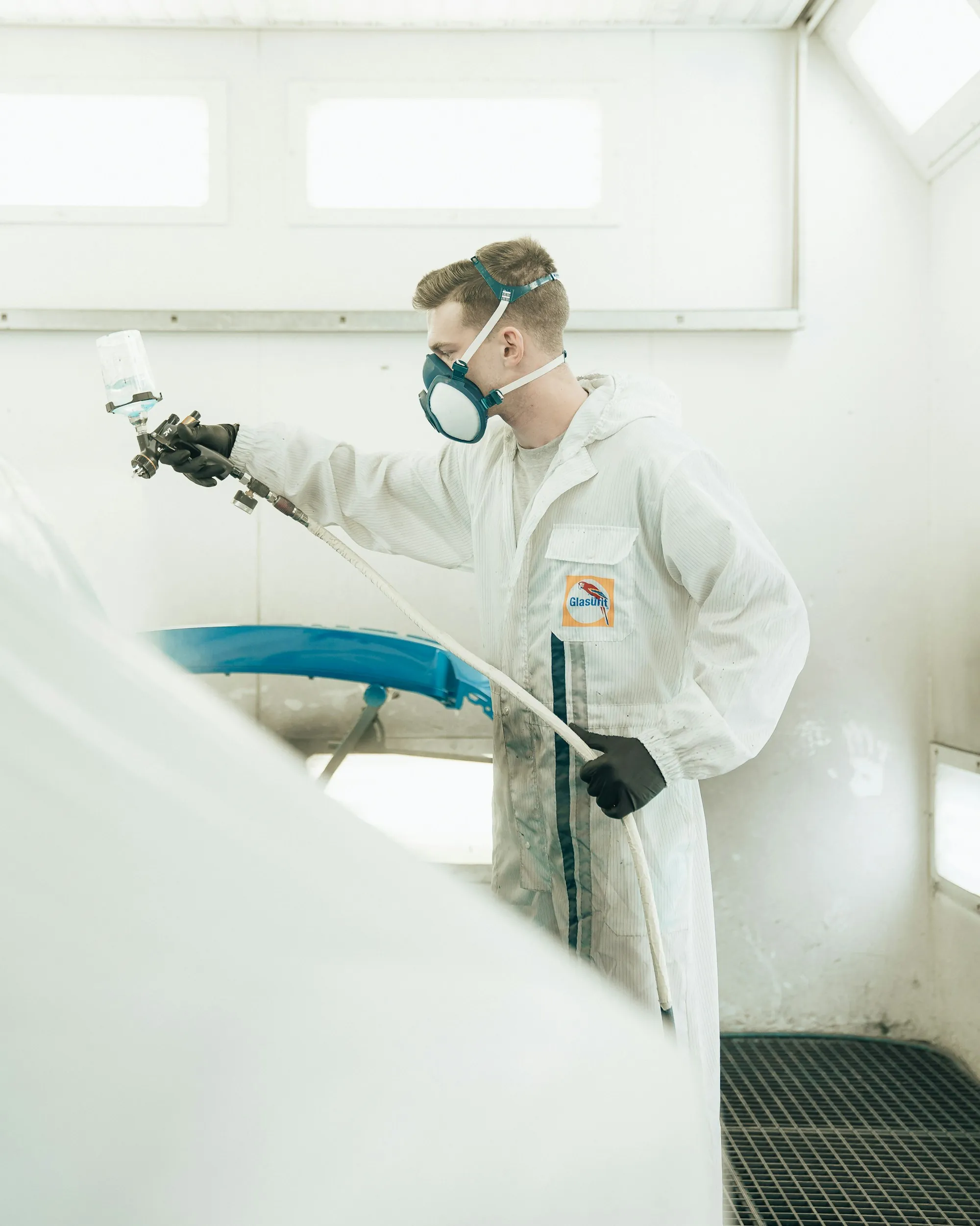 Painter in a protective suit spraying a car inside a paint booth